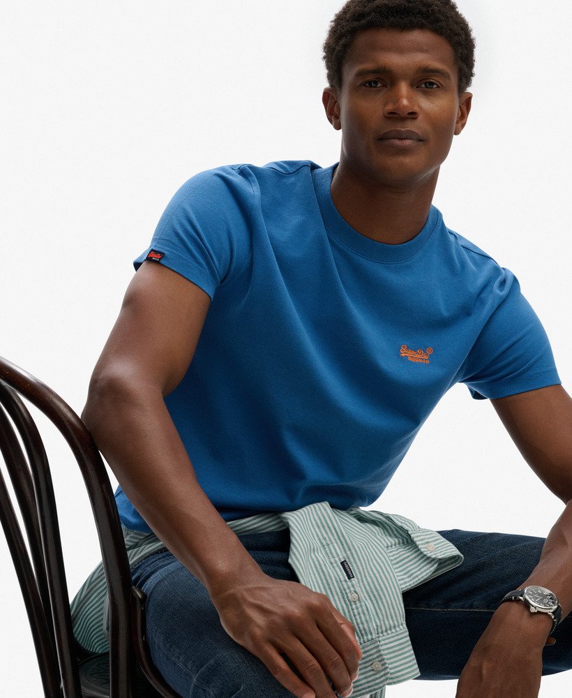 Man wearing a blue t-shirt with a logo, sitting on a chair against a white background