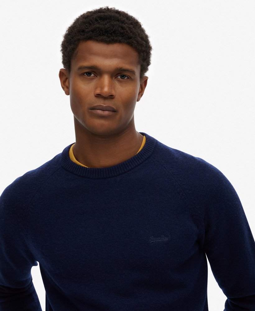 Man wearing a navy sweater with a brand logo on a white background