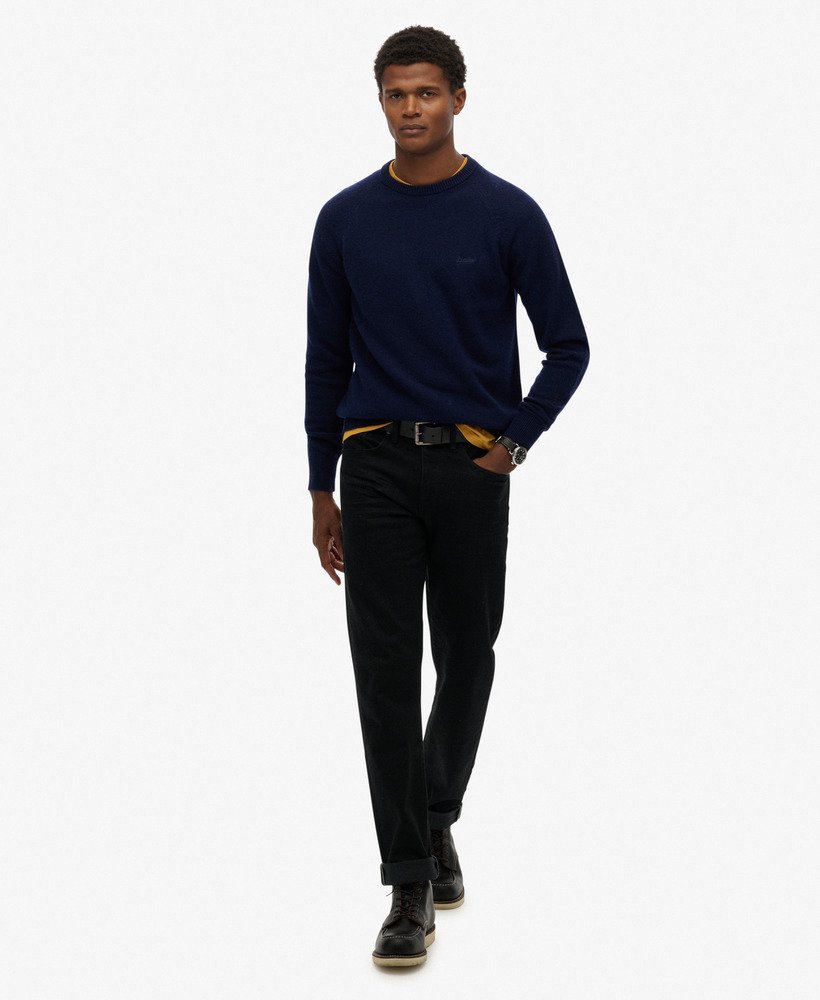 Man wearing a navy sweater and black pants on a white background