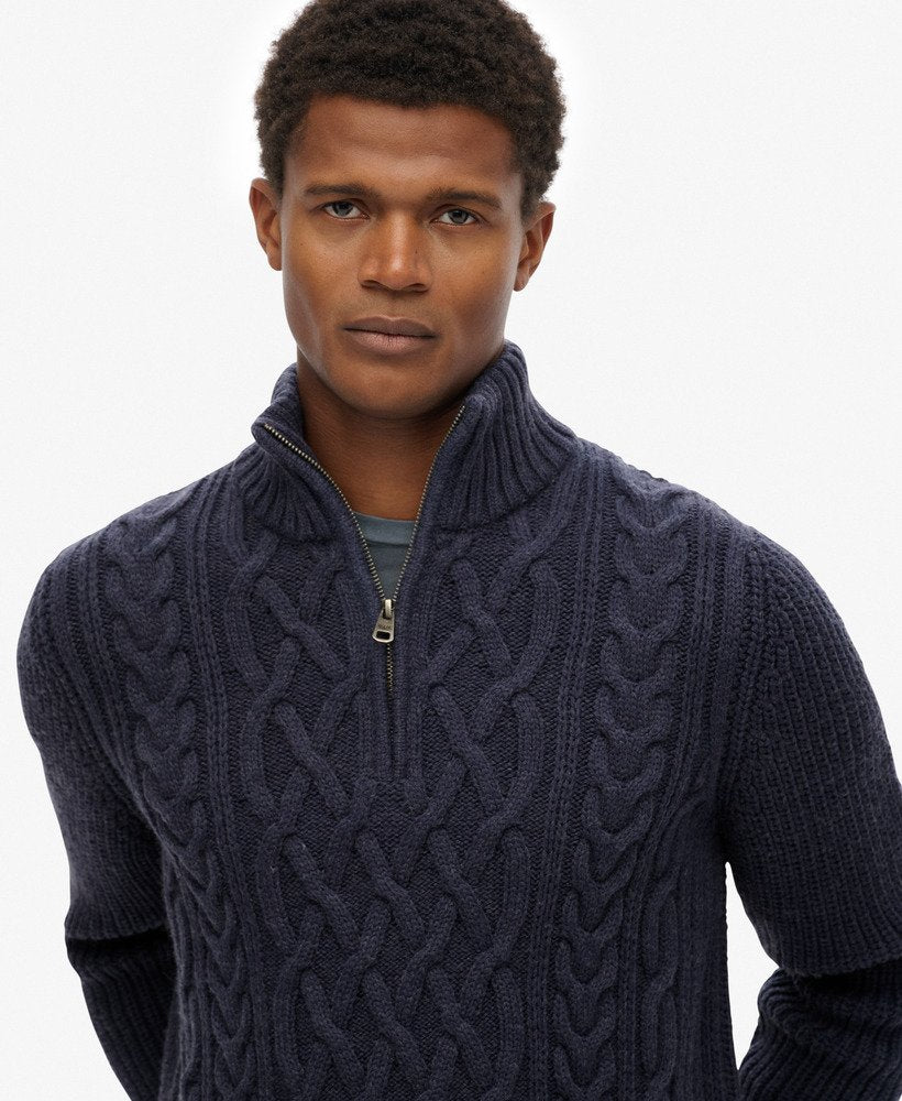 Man wearing a dark blue cable knit sweater with a white background