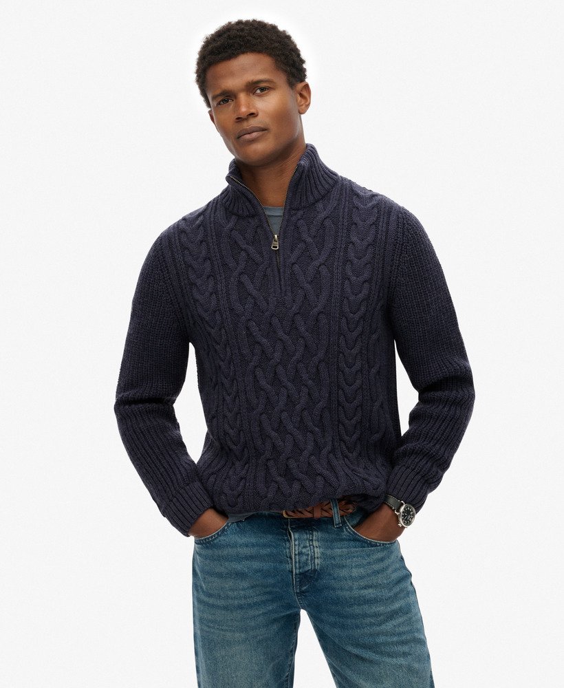 Man wearing a dark blue cable knit sweater with a white background