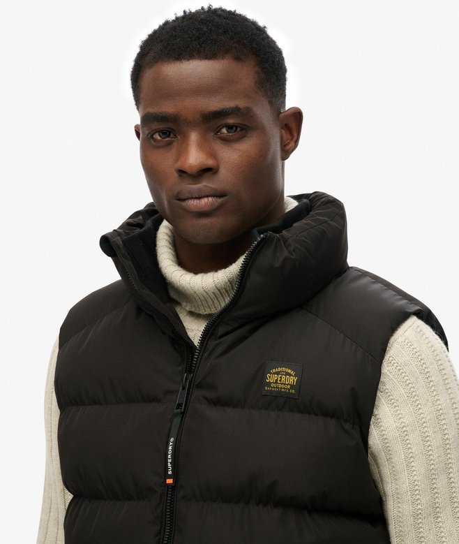 Man wearing a black puffer vest with a visible brand logo on a white background