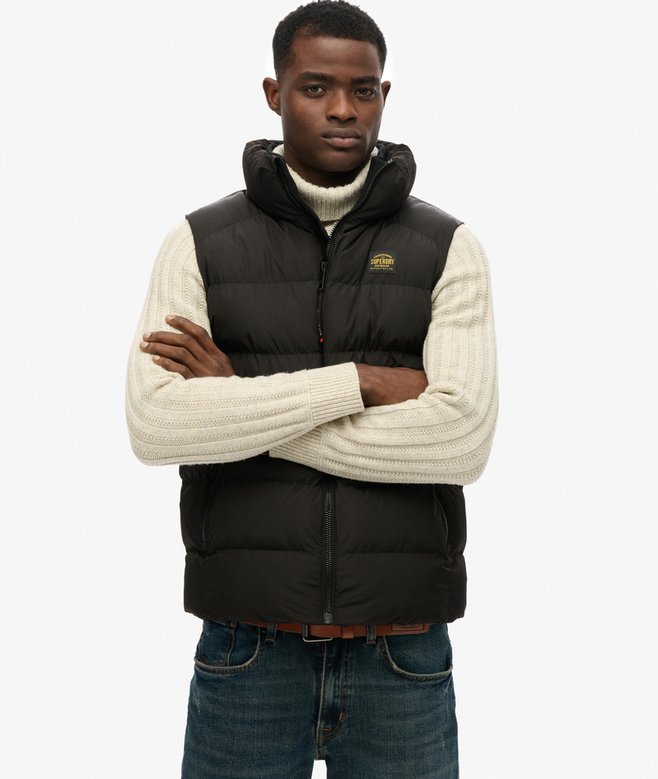 Man wearing a black puffer vest over a cream sweater on a white background