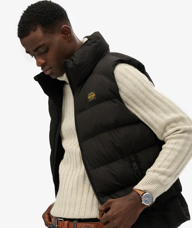 Man wearing a black puffer vest over a cream sweater on a white background