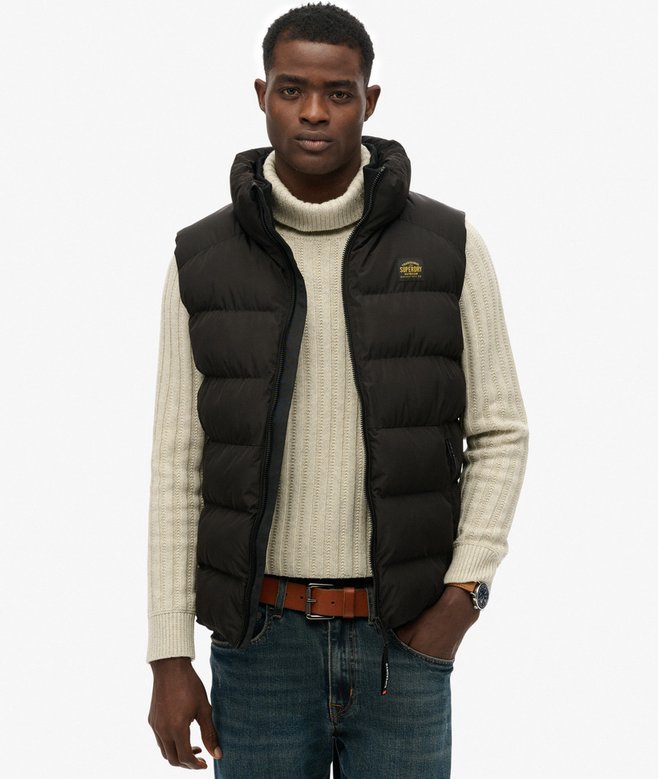 Man wearing a black puffer vest over a cream sweater on a white background