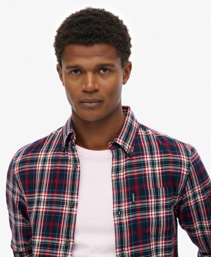 Man wearing a plaid shirt over a white shirt on a plain background