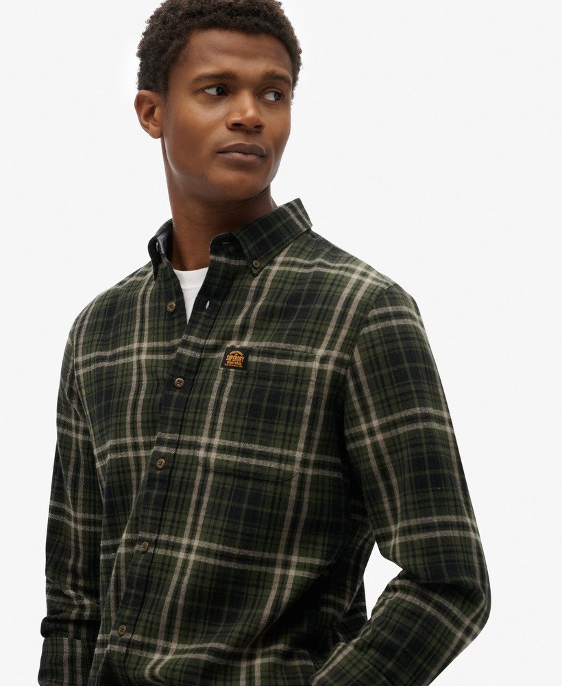 Man wearing a plaid shirt over a white t-shirt with a visible brand logo on a white background