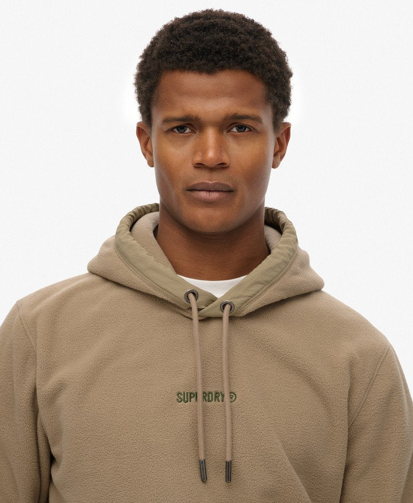 Man wearing a beige hoodie with a brand logo on a white background