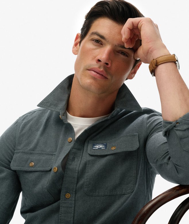 Man wearing a green shirt with a brand logo, sitting on a chair against a white background