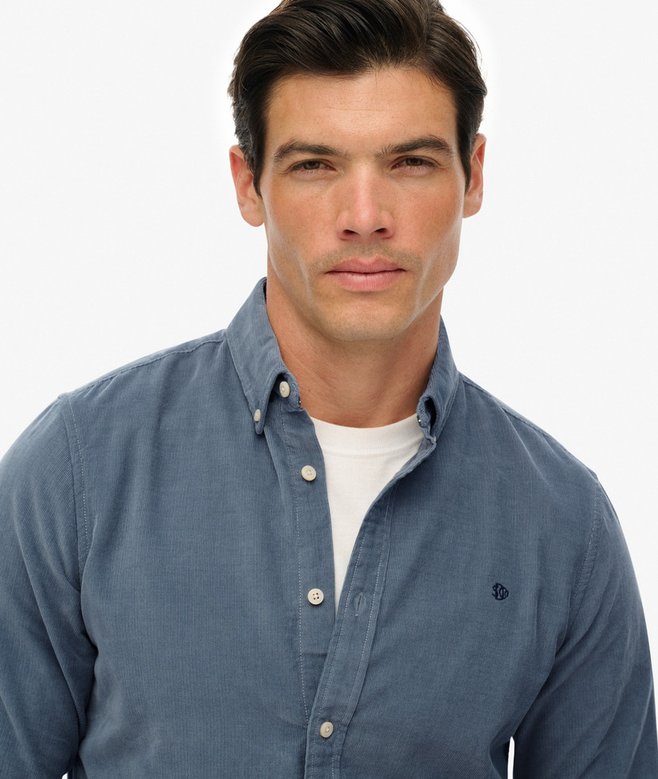 Man wearing a blue button-up shirt over a white shirt on a plain background