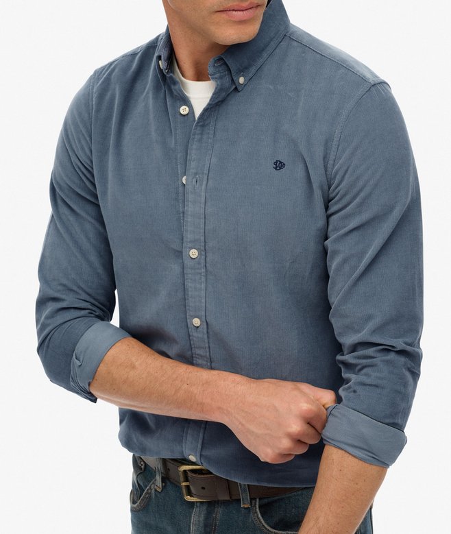 Man wearing a blue button-up shirt with rolled-up sleeves on a white background
