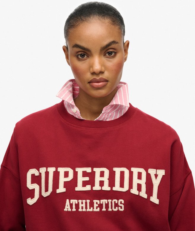 Person wearing a red Superdry Athletics sweatshirt with a white background