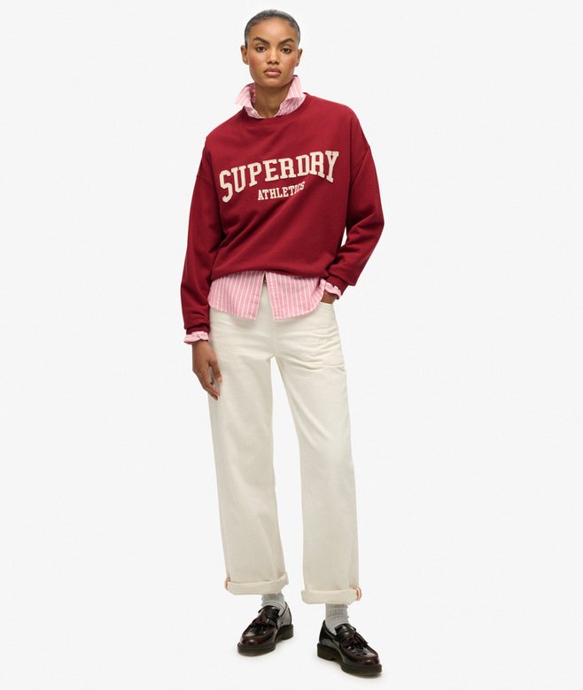 Person wearing a red Superdry sweatshirt with white pants on a white background