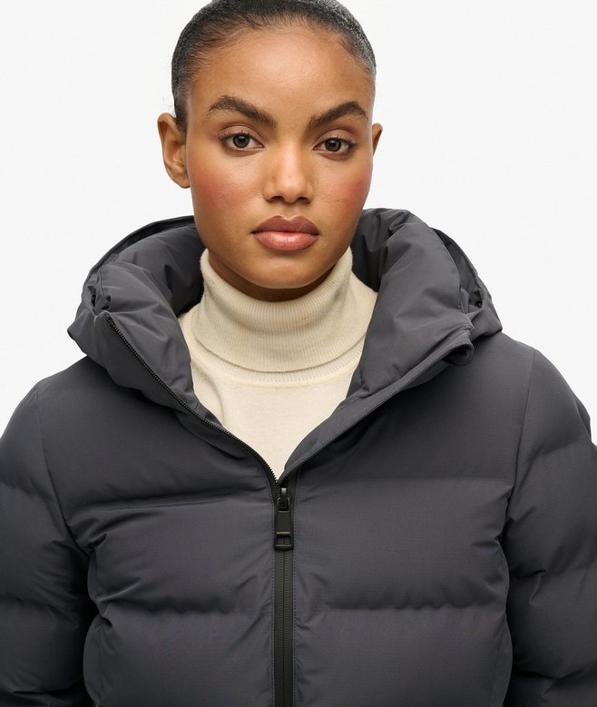 Person wearing a black puffer jacket over a beige turtleneck on a white background