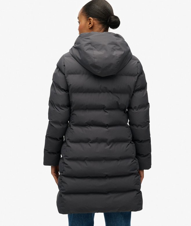 Person wearing a long dark gray puffer coat on a white background