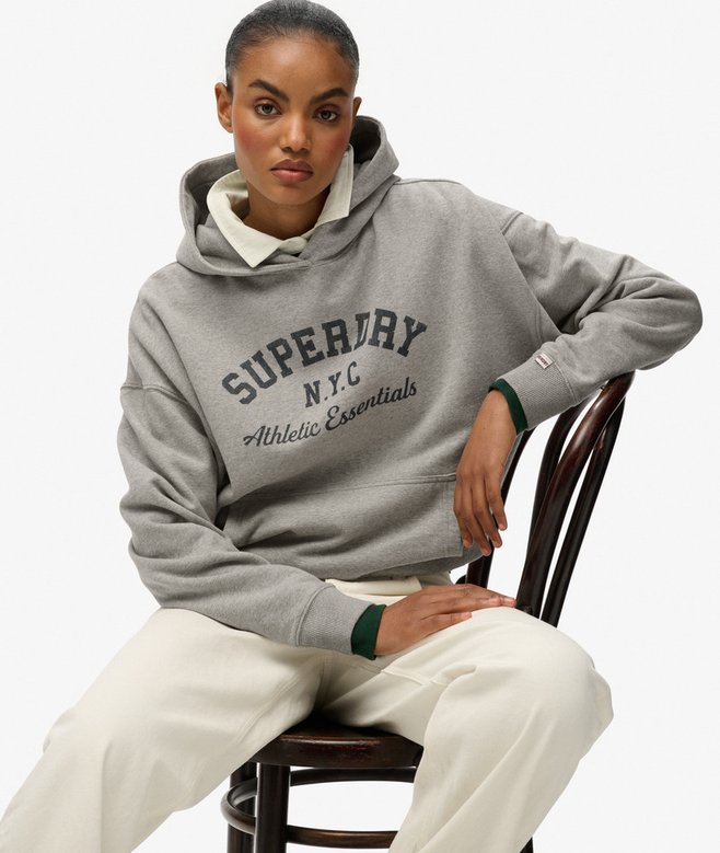 Person wearing a gray hoodie with 'Superdry' branding, sitting on a chair.