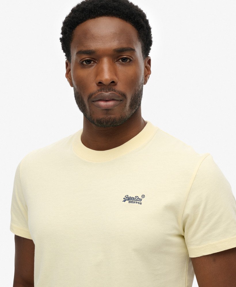 Man wearing a light yellow t-shirt with a brand logo on a white background