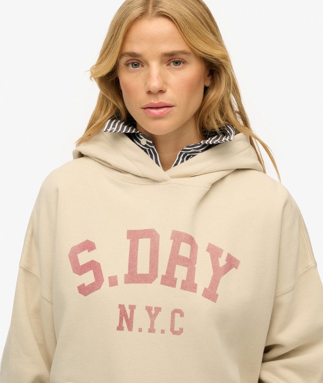 Woman wearing a beige hoodie with 'S. DRY N.Y.C.' text on a plain background