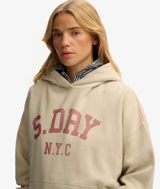 Woman wearing a beige hoodie with 'S.DRY N.Y.C.' text on a plain background