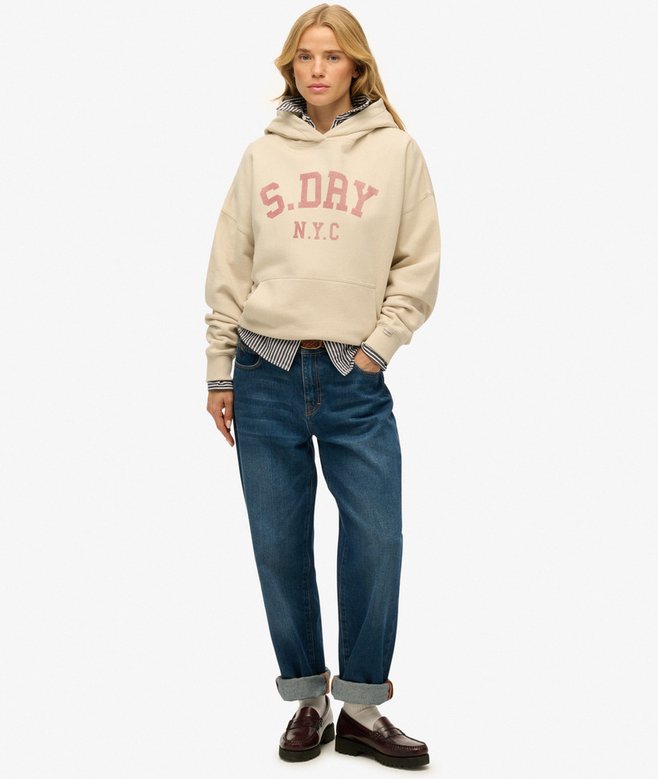 Person wearing a beige hoodie with 'S. DRY N.Y.C.' text, blue jeans, and brown shoes on a white background