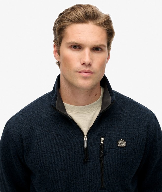 Man wearing a navy blue quarter-zip sweater with a logo on a white background