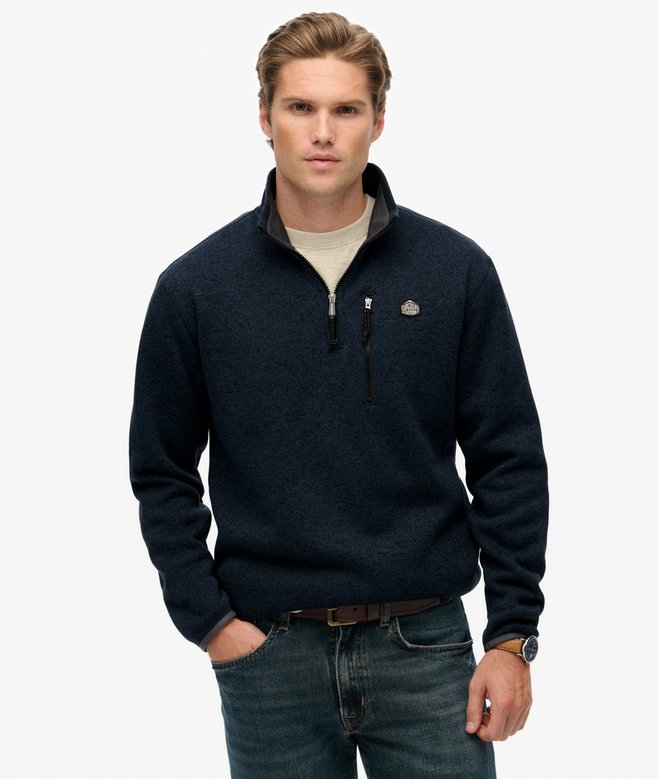 Man wearing a navy blue pullover with a logo on a white background