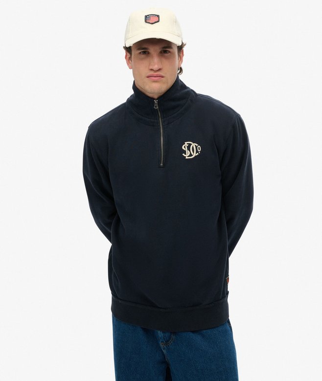 Man wearing a navy half-zip sweatshirt with a logo on a white background