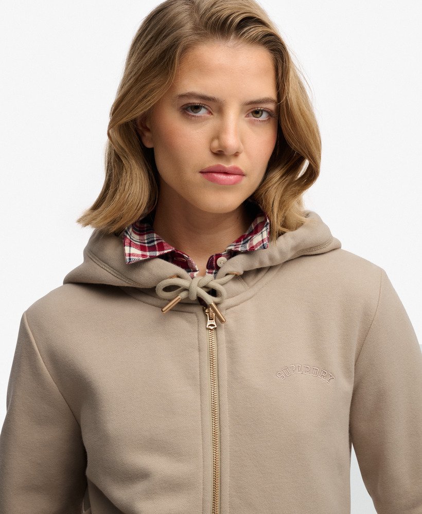 Woman wearing a beige hoodie with a plaid shirt underneath on a white background