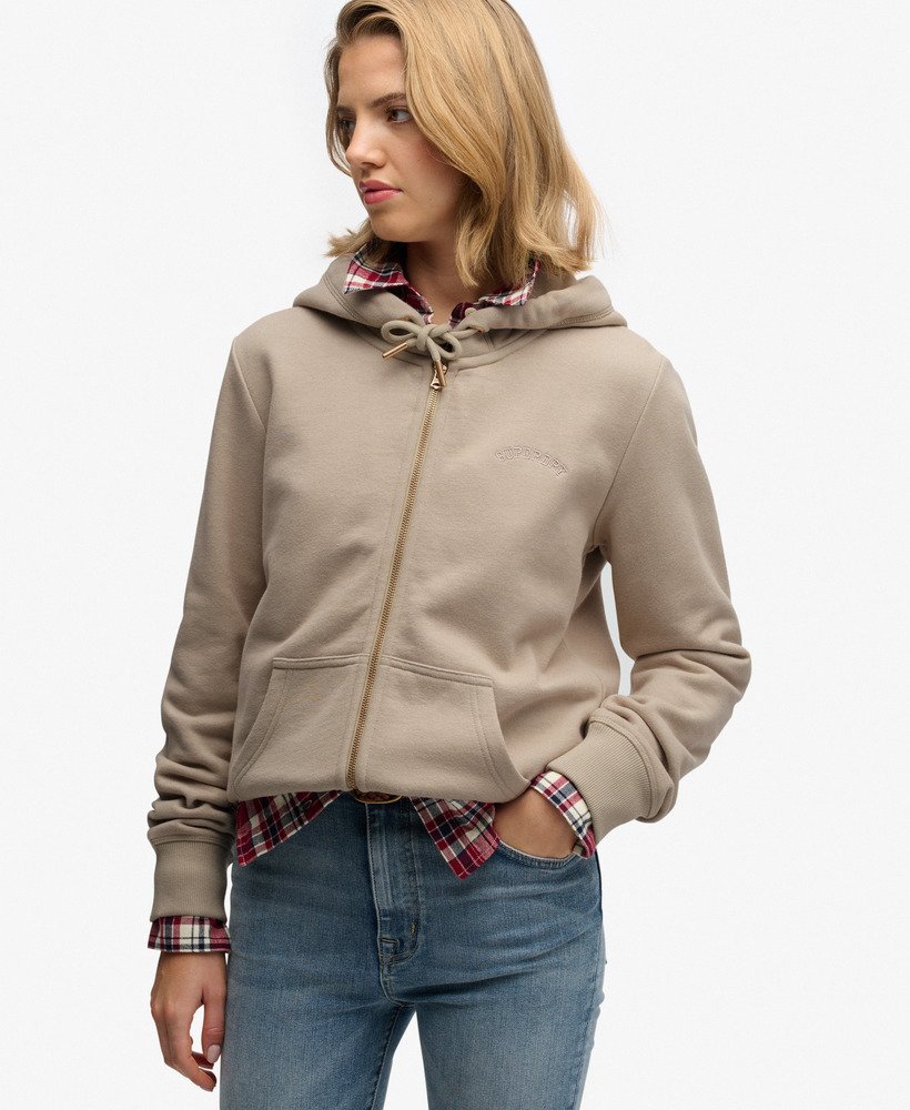 Woman wearing a beige hoodie with a plaid shirt and blue jeans on a white background