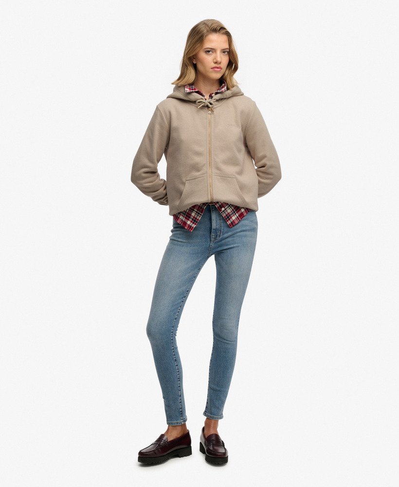 Woman wearing a beige hoodie and blue jeans on a white background