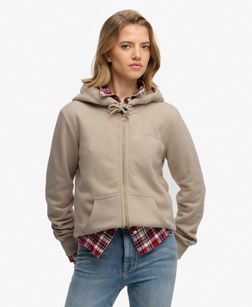 Woman wearing a beige hoodie over a plaid shirt with a white background