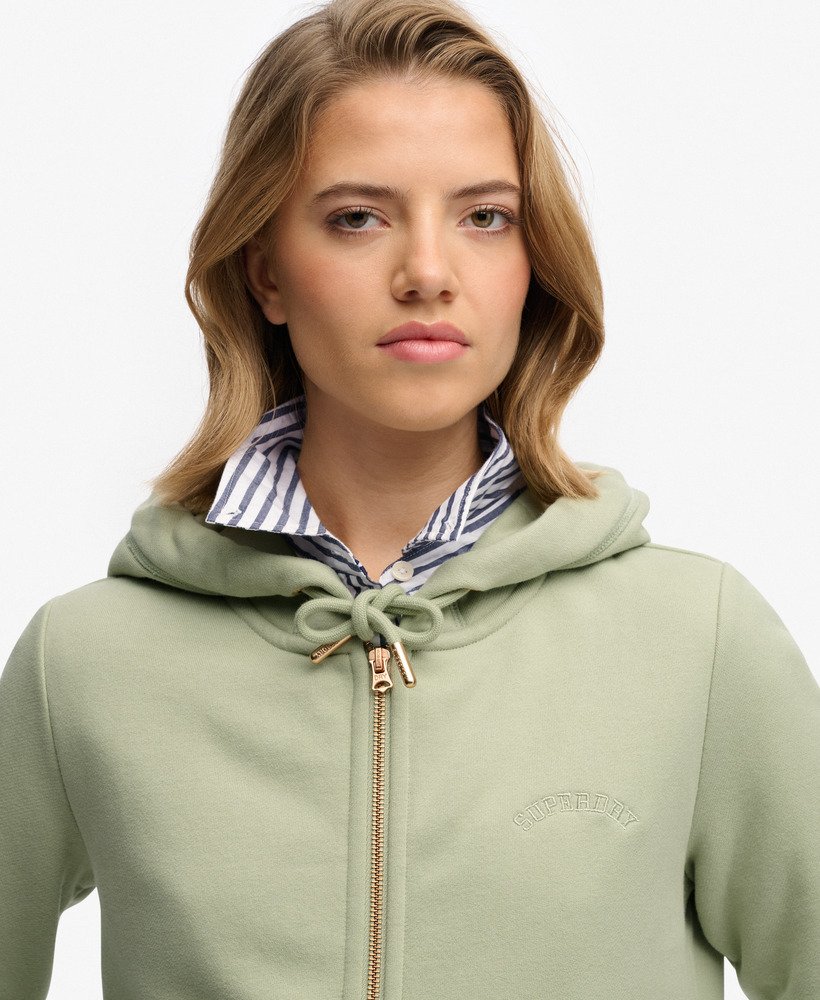 Woman wearing a light green hoodie with a brand logo on a white background