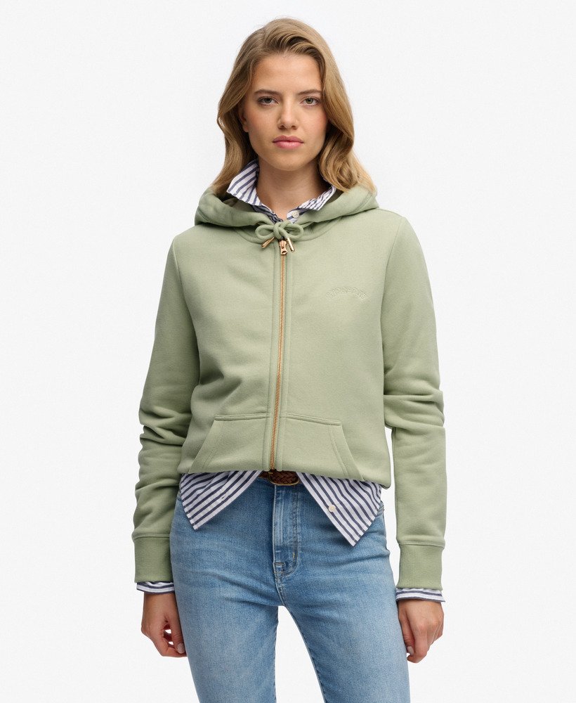 Woman wearing a green hoodie over a striped shirt with blue jeans on a white background