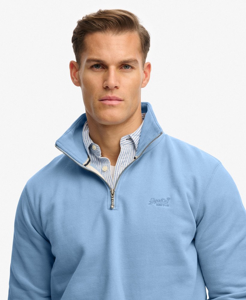 Man wearing a light blue pullover with a brand logo on a white background