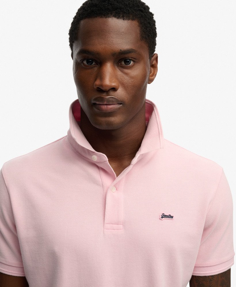 Man wearing a pink polo shirt with a brand logo on a white background