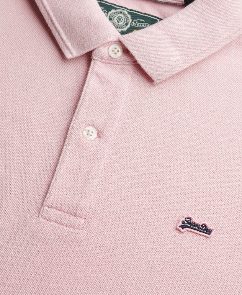 Close-up of a pink polo shirt with a brand logo on a light pink background
