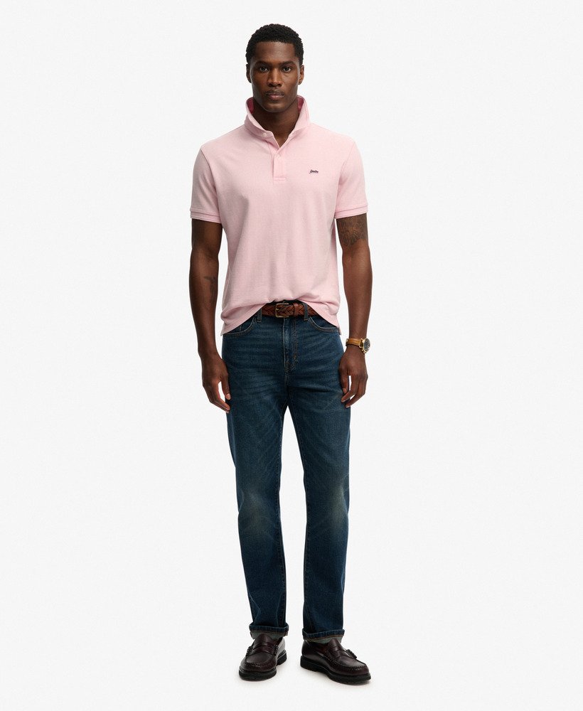 Man wearing a pink polo shirt and dark jeans on a white background