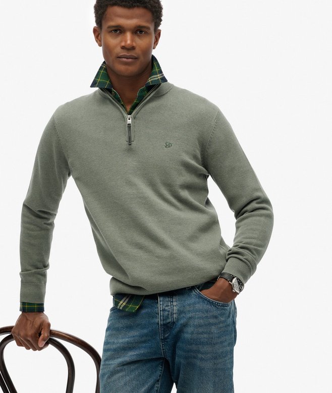 Man wearing a green quarter-zip sweater and blue jeans on a white background