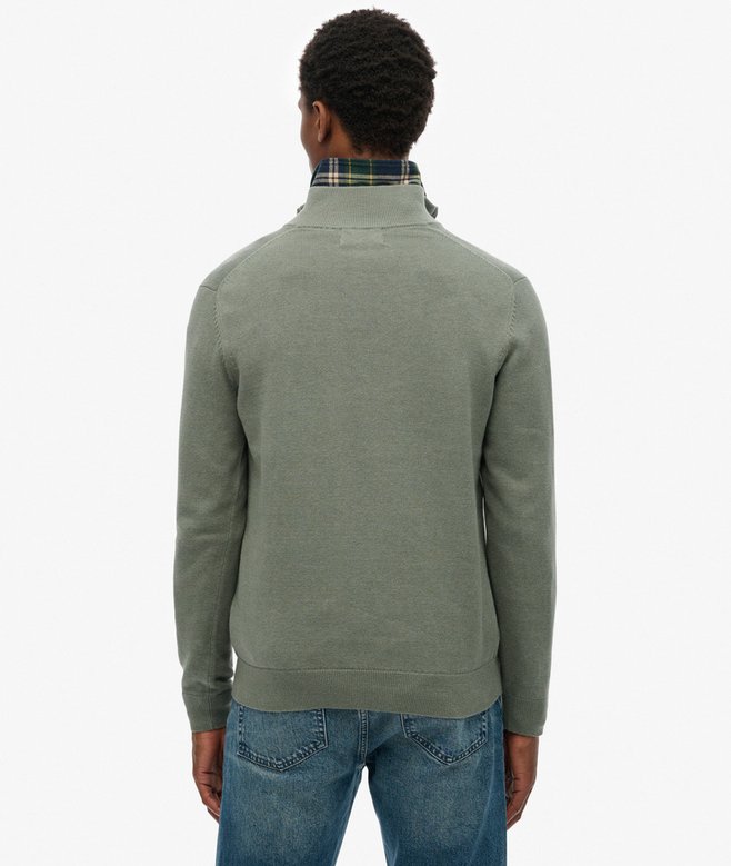 Person wearing a green half-zip sweater and blue jeans on a white background