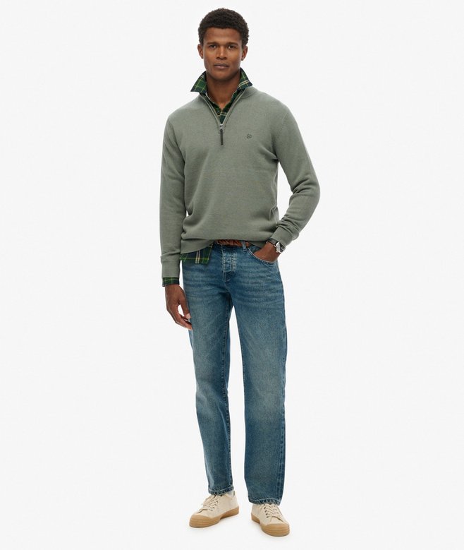 Man wearing a green sweater and blue jeans on a white background