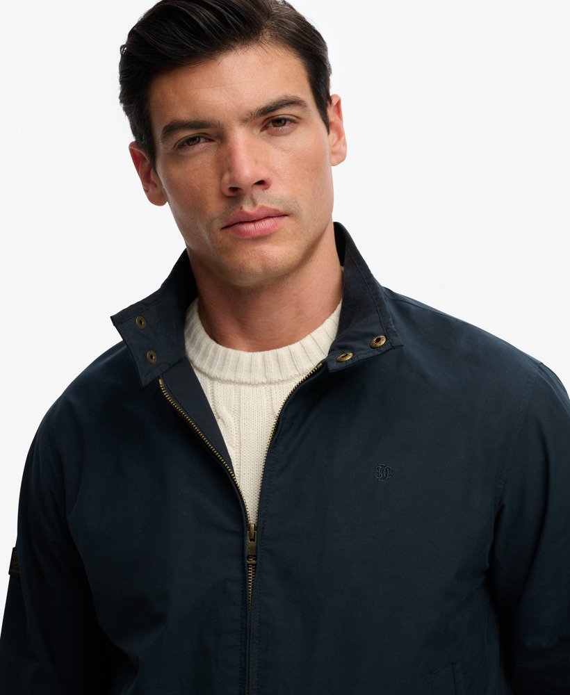 Man wearing a navy jacket over a white sweater on a plain background