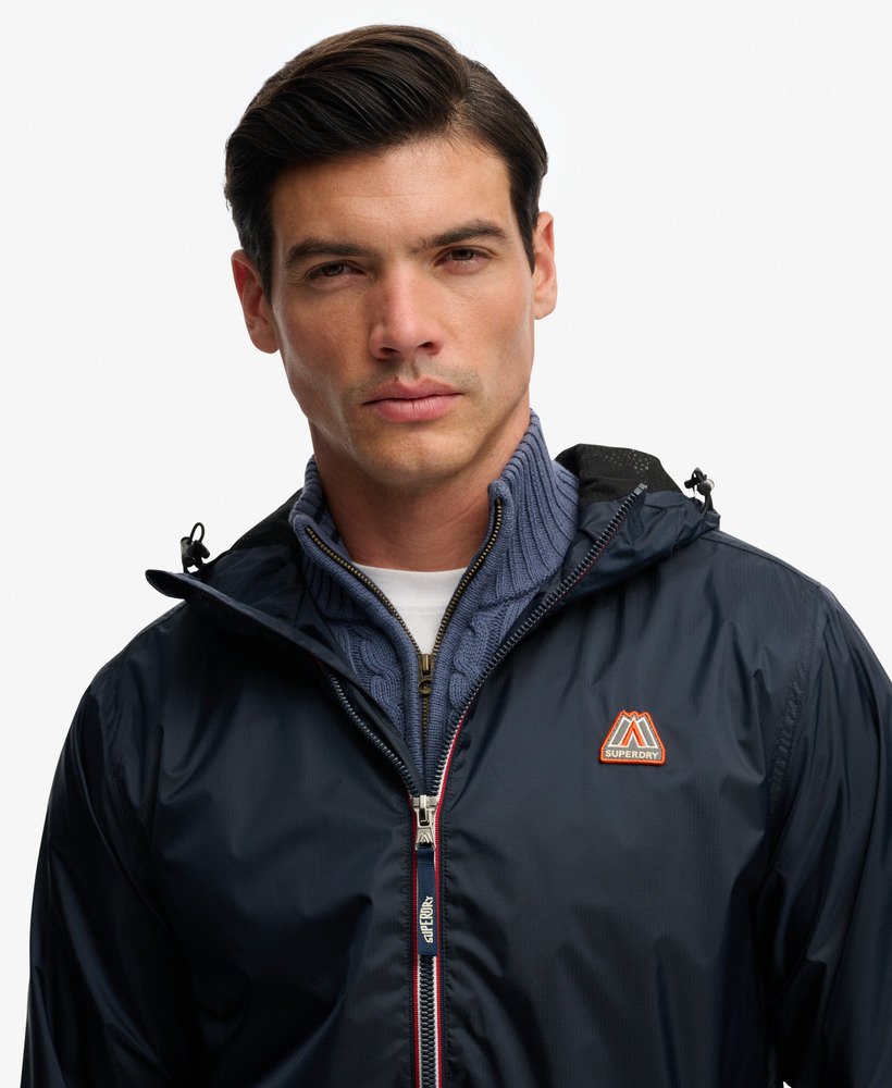 Man wearing a navy jacket with a brand logo on a light gray background