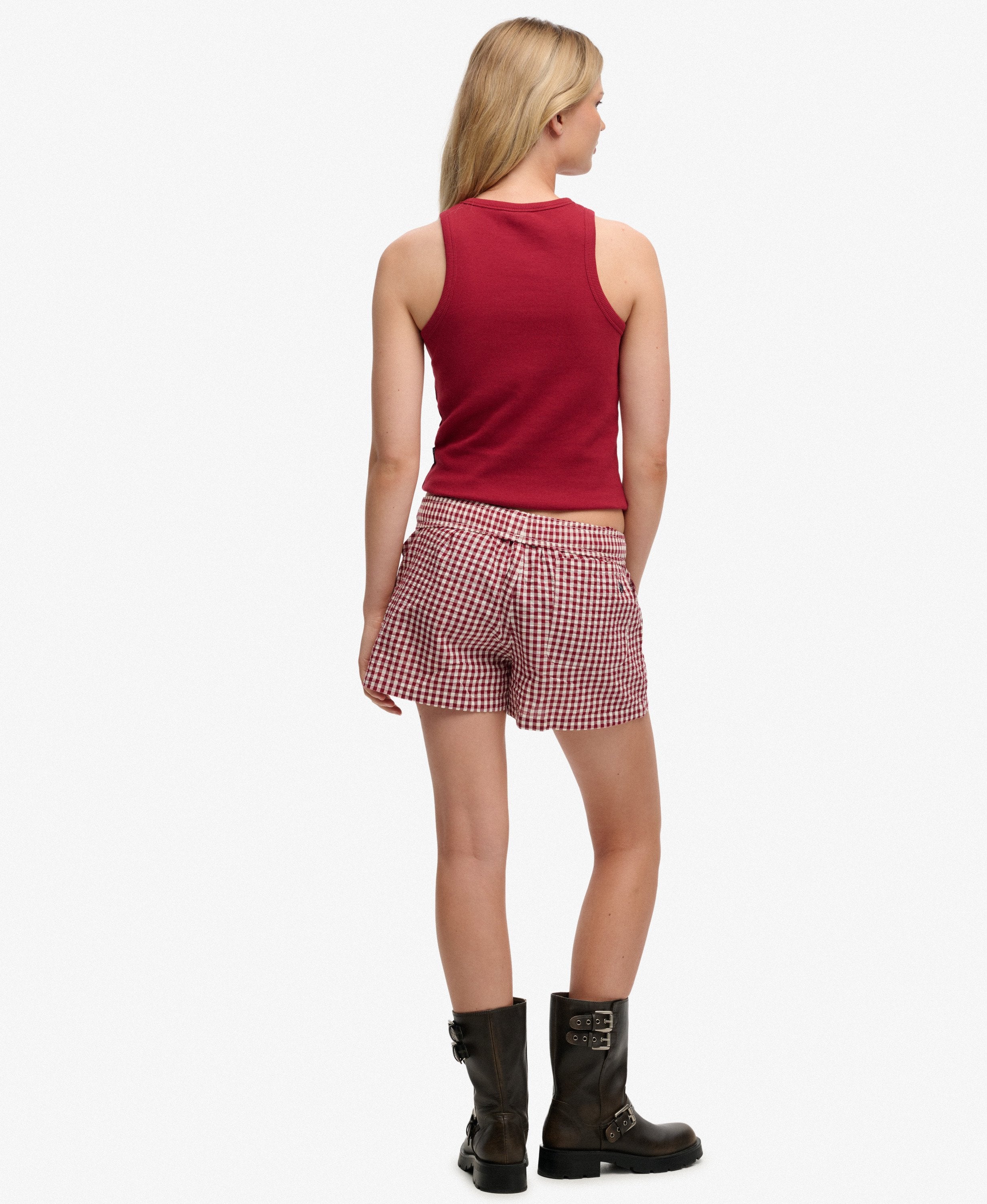 Woman wearing a red sleeveless top and checkered shorts on a white background
