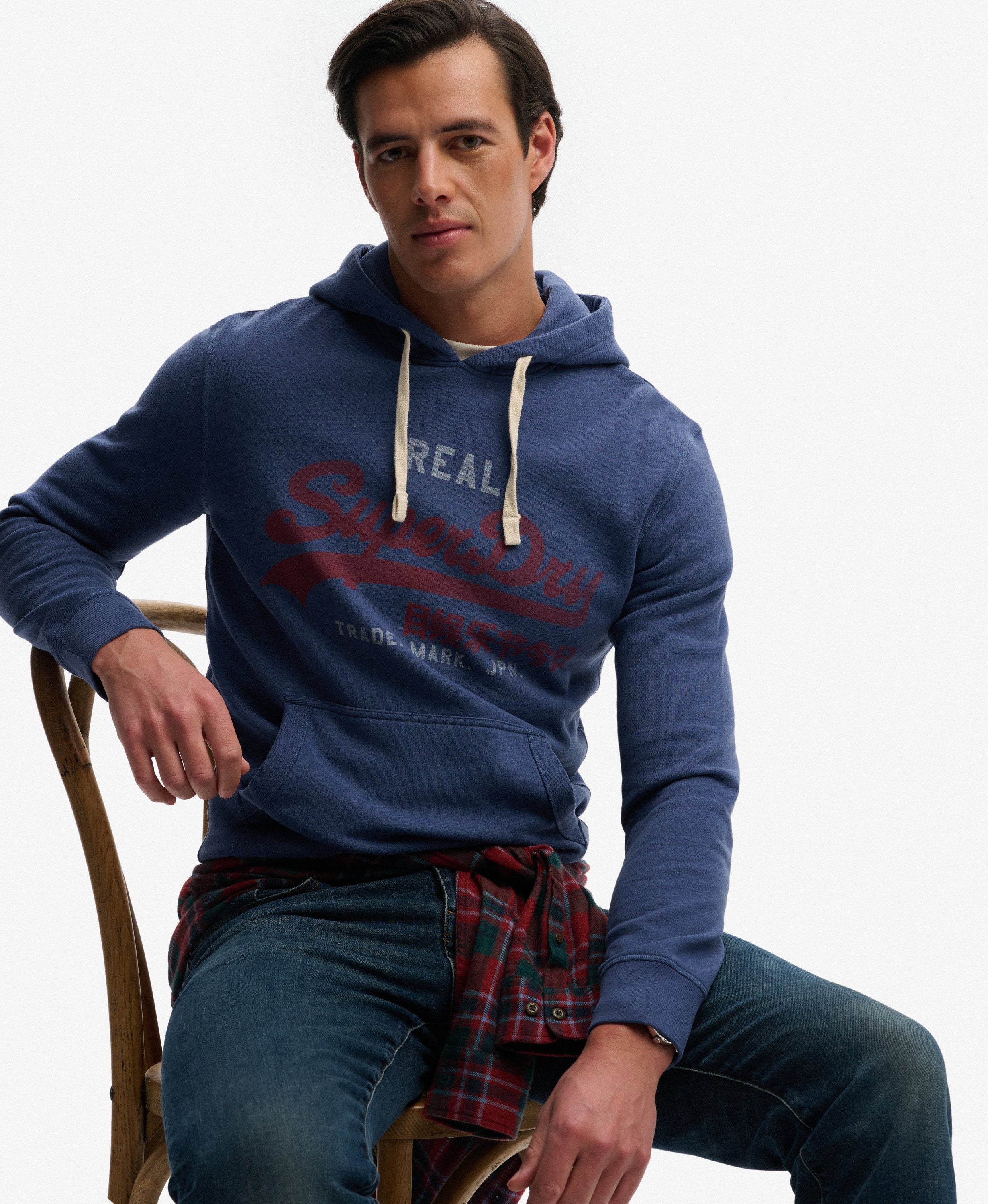 Man wearing a blue hoodie with visible branding, sitting on a chair against a white background