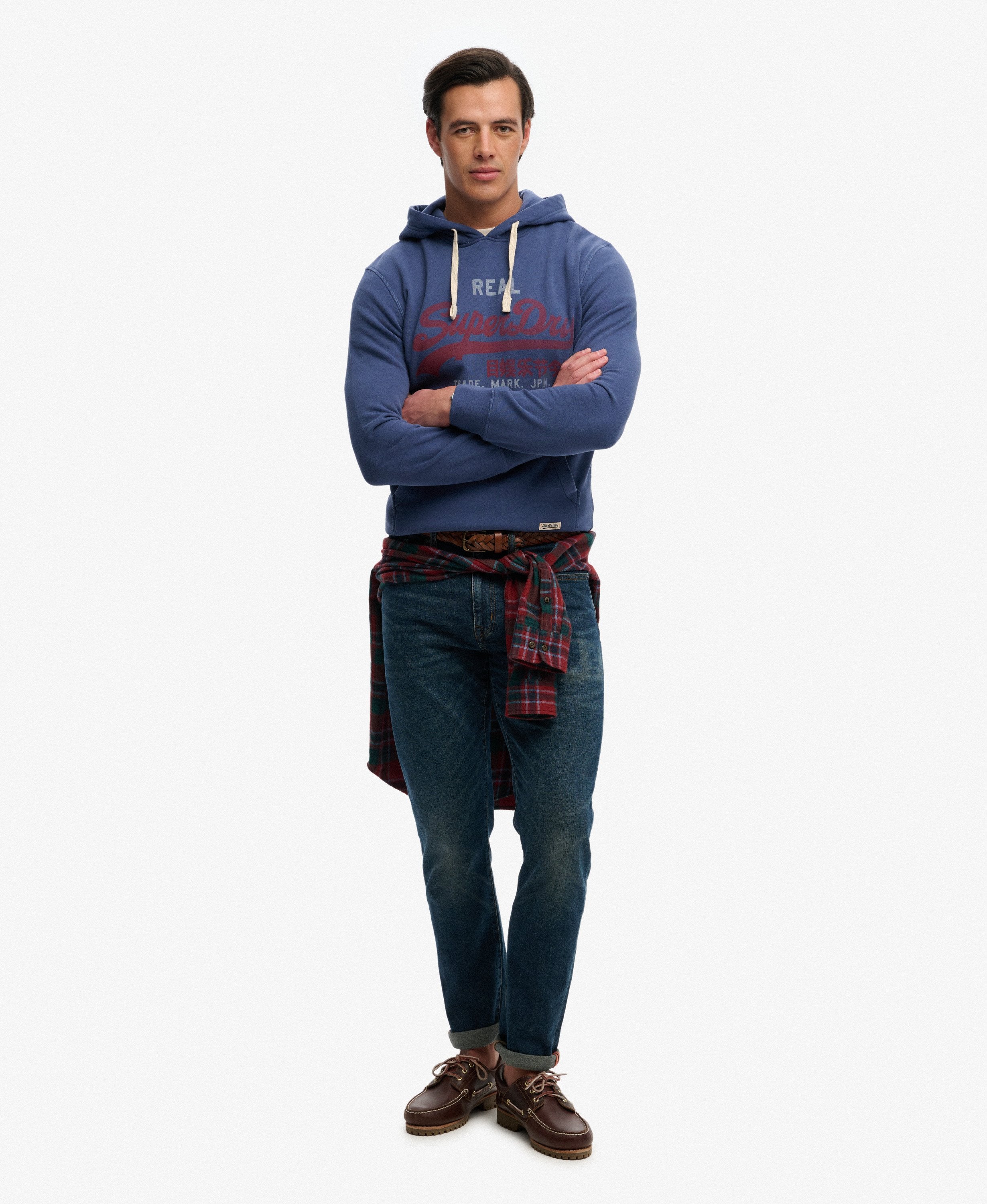 Man wearing a blue hoodie with a brand logo, plaid shirt, and jeans on a white background
